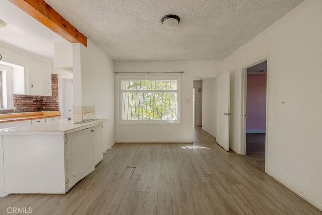 kitchen featuring light countertops, white cabinets, light wood-style floors, beamed ceiling, and backsplash