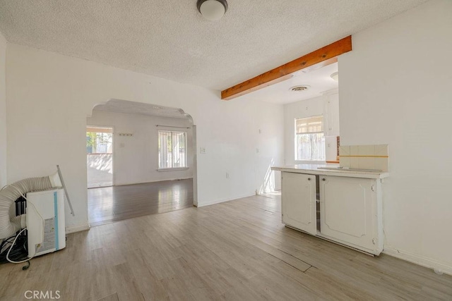 spare room featuring beam ceiling, plenty of natural light, arched walkways, and light wood finished floors