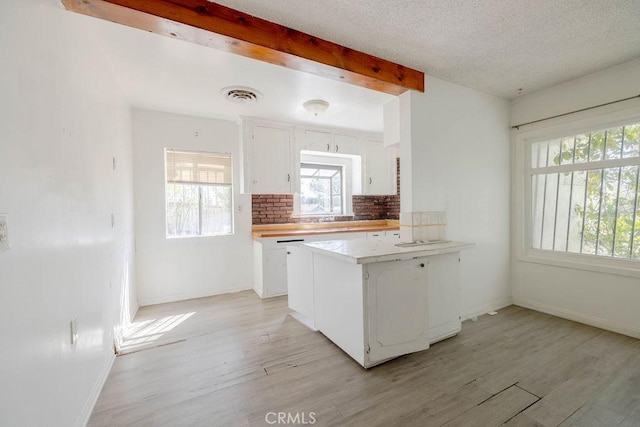 kitchen featuring visible vents, beamed ceiling, light wood-style flooring, tasteful backsplash, and white cabinetry