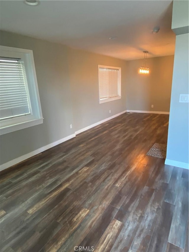 spare room featuring dark wood-style floors, a chandelier, and baseboards