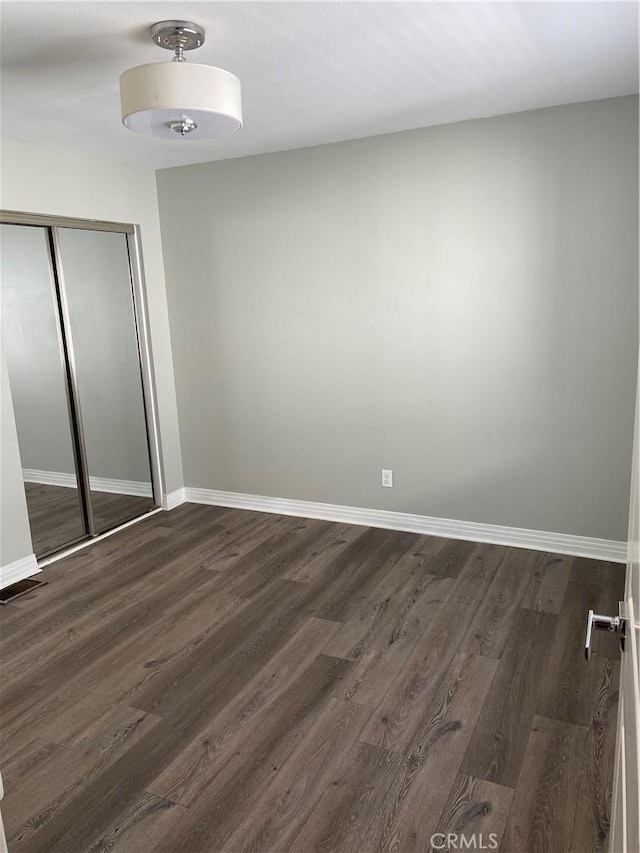 unfurnished bedroom featuring a closet, dark wood finished floors, visible vents, and baseboards