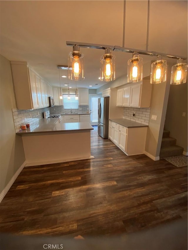 kitchen with stainless steel appliances, dark wood-type flooring, white cabinets, a sink, and a peninsula