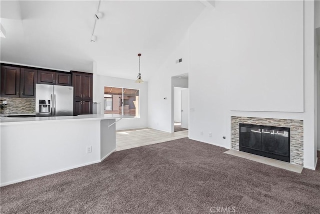 unfurnished living room featuring rail lighting, visible vents, a fireplace with flush hearth, light carpet, and high vaulted ceiling