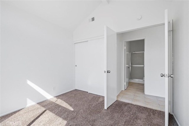 unfurnished bedroom featuring light tile patterned floors, visible vents, light colored carpet, vaulted ceiling, and a closet