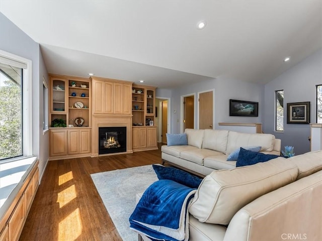 living room featuring dark wood-style floors, a glass covered fireplace, vaulted ceiling, and recessed lighting