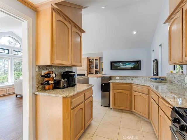 kitchen with lofted ceiling, decorative backsplash, gas stove, light stone countertops, and a peninsula