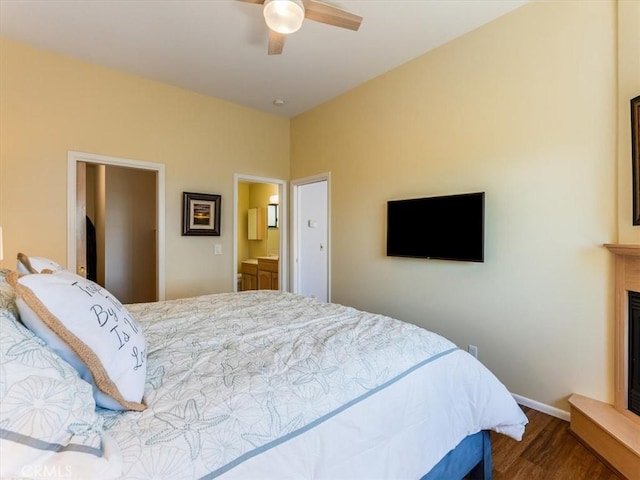 bedroom with connected bathroom, a fireplace, wood finished floors, a ceiling fan, and baseboards