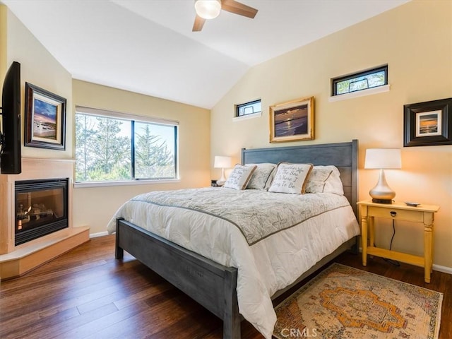 bedroom with lofted ceiling, a glass covered fireplace, baseboards, and wood finished floors