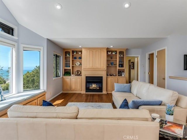 living room with dark wood-style floors, vaulted ceiling, a glass covered fireplace, and recessed lighting