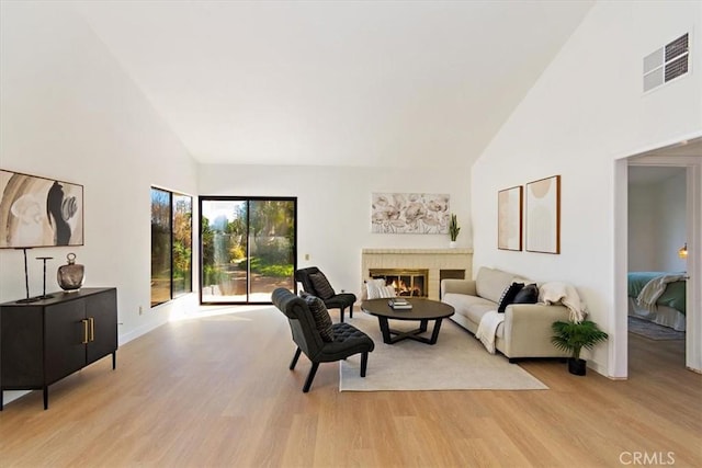 living area with high vaulted ceiling, visible vents, a fireplace, and light wood finished floors