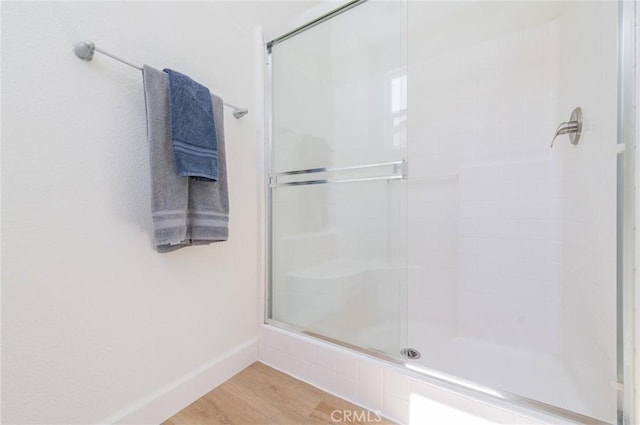 bathroom featuring wood finished floors, a stall shower, and baseboards