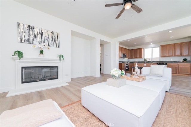 living room with a glass covered fireplace, recessed lighting, light wood finished floors, baseboards, and ceiling fan