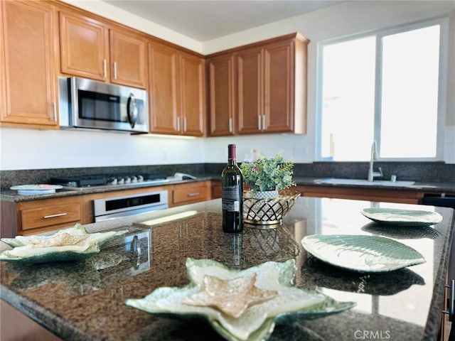 kitchen with oven, dark stone countertops, stainless steel microwave, a sink, and stovetop