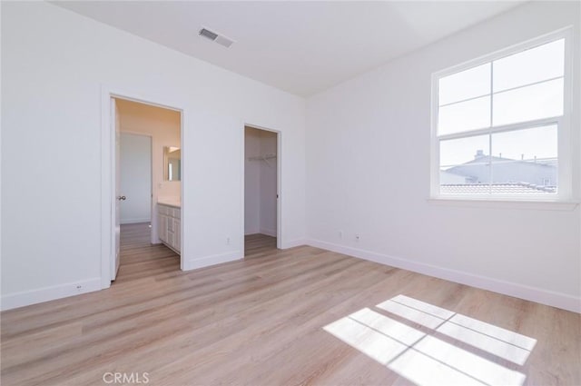 unfurnished bedroom with light wood finished floors, visible vents, a spacious closet, and baseboards