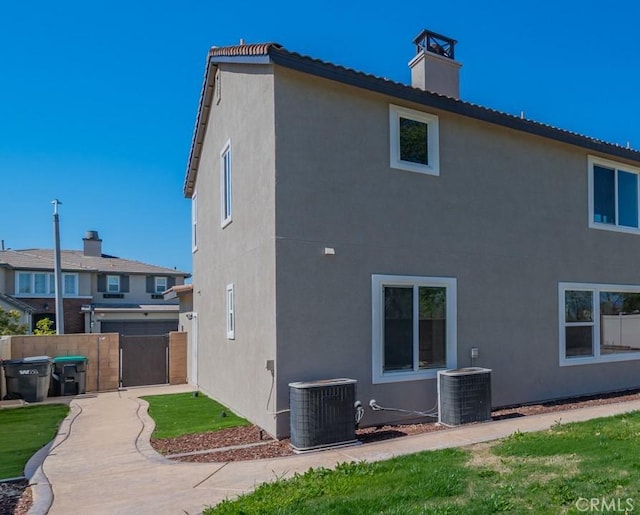 back of property with stucco siding, cooling unit, and a gate