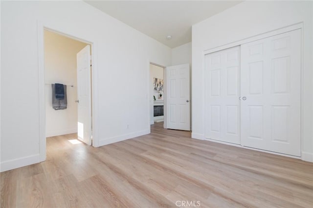 unfurnished bedroom featuring light wood-style flooring, baseboards, and a closet