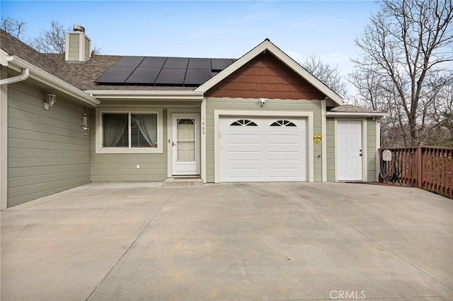 exterior space featuring an attached garage, solar panels, concrete driveway, roof with shingles, and a chimney