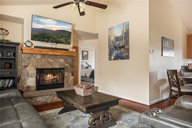 living area featuring high vaulted ceiling, a fireplace, wood finished floors, a ceiling fan, and baseboards