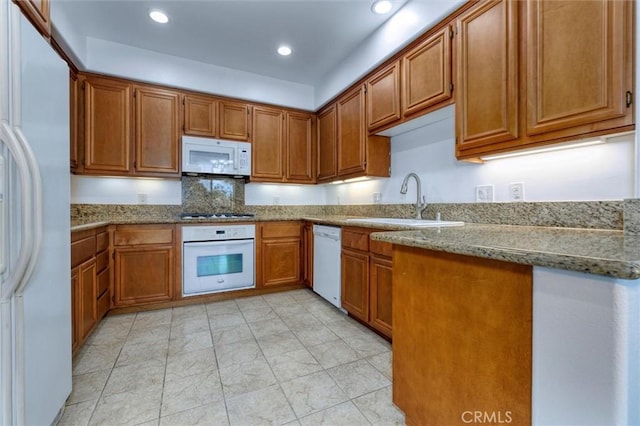 kitchen featuring white appliances, brown cabinetry, a sink, and light stone countertops