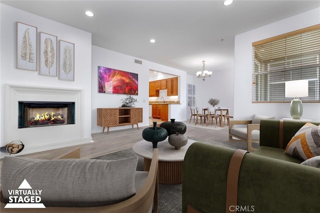 living area with a chandelier, recessed lighting, visible vents, a lit fireplace, and light wood finished floors