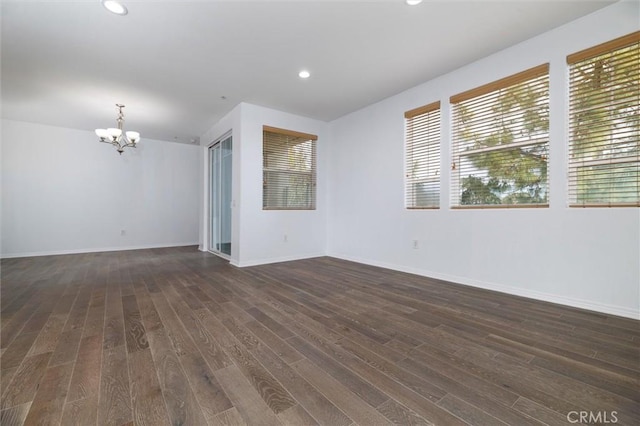 spare room featuring dark wood-type flooring, recessed lighting, baseboards, and an inviting chandelier