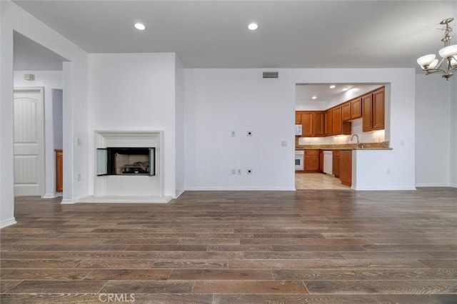 unfurnished living room with a chandelier, a fireplace with raised hearth, dark wood-type flooring, a sink, and visible vents