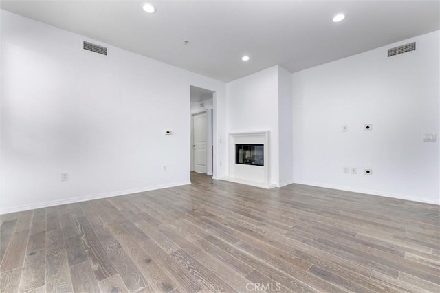 unfurnished living room with recessed lighting, visible vents, wood finished floors, and a glass covered fireplace