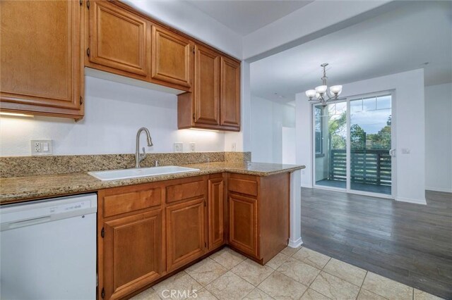 kitchen with light stone counters, brown cabinets, an inviting chandelier, white dishwasher, and a sink