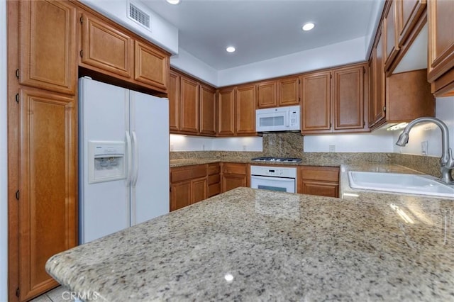 kitchen featuring recessed lighting, white appliances, a sink, visible vents, and brown cabinetry