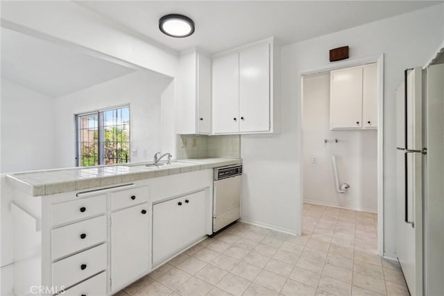 kitchen with white appliances, a peninsula, a sink, decorative backsplash, and white cabinetry