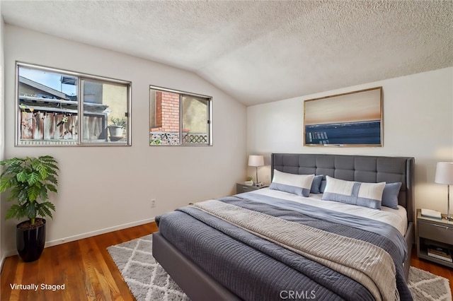 bedroom featuring vaulted ceiling, a textured ceiling, baseboards, and wood finished floors