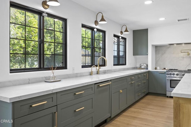 kitchen featuring gray cabinetry, a sink, visible vents, light stone countertops, and stainless steel range