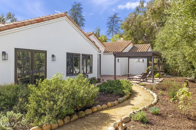 back of house featuring stucco siding, a tile roof, a chimney, and a patio