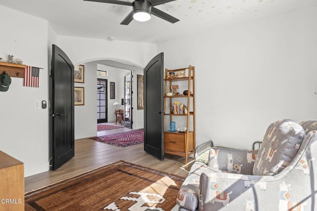 sitting room with arched walkways, ceiling fan, wood finished floors, and baseboards