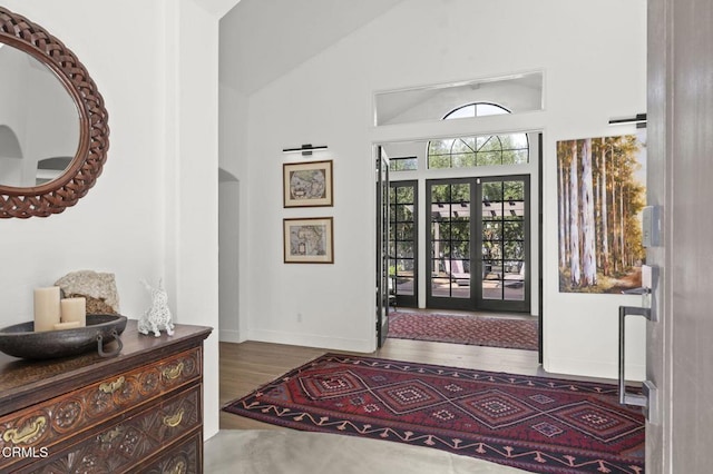 entryway featuring arched walkways, french doors, lofted ceiling, wood finished floors, and baseboards