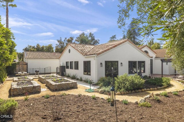 back of property with a vegetable garden, a tile roof, a gate, fence, and stucco siding