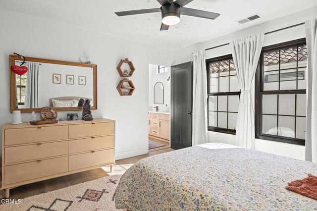 bedroom with ensuite bathroom, ceiling fan, visible vents, baseboards, and light wood finished floors