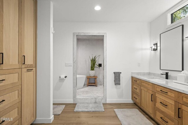 full bath featuring a freestanding bath, wood finished floors, vanity, and baseboards