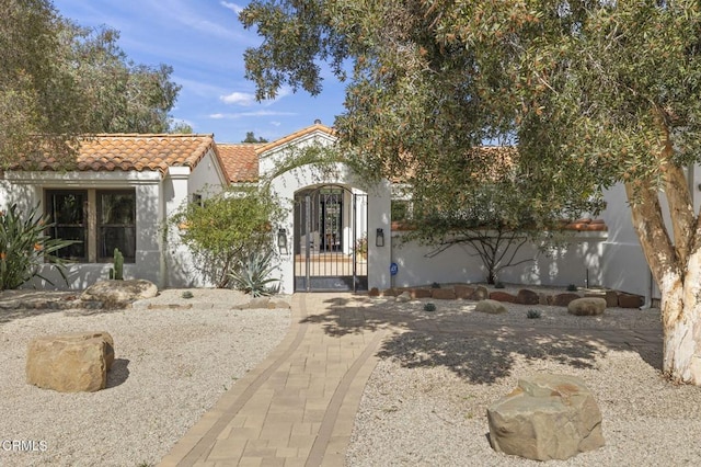 mediterranean / spanish home featuring a fenced front yard, a tile roof, a gate, and stucco siding