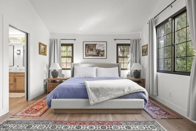 bedroom featuring multiple windows, ensuite bath, and wood finished floors