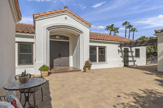 doorway to property featuring a patio, stucco siding, a tile roof, and a pergola