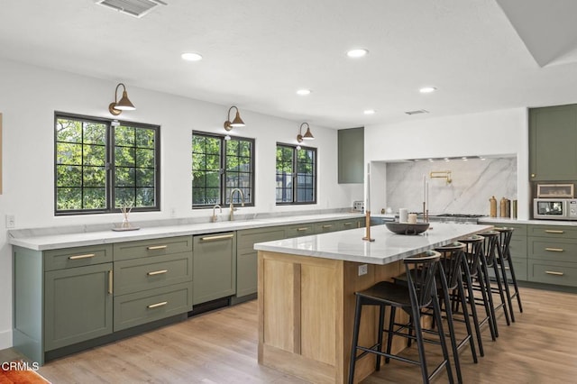 kitchen with light wood finished floors, green cabinetry, visible vents, stainless steel microwave, and light stone countertops