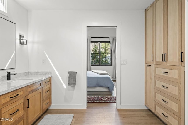 ensuite bathroom featuring wood finished floors, vanity, baseboards, and connected bathroom