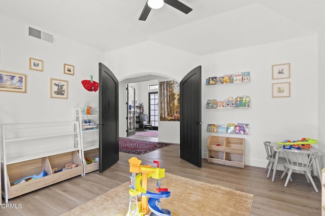 recreation room with a ceiling fan, wood finished floors, arched walkways, baseboards, and visible vents