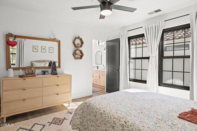 bedroom featuring light wood finished floors, multiple windows, visible vents, and ensuite bathroom