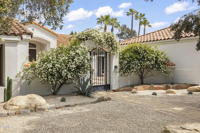 property entrance featuring a gate, a tiled roof, stucco siding, and fence