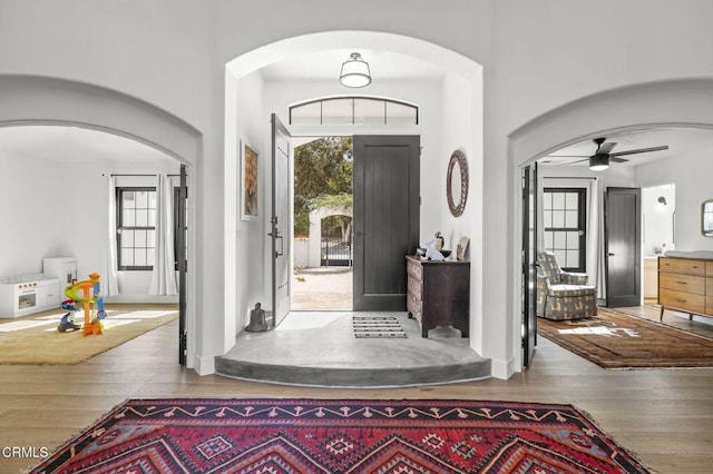 foyer entrance with a towering ceiling, wood finished floors, arched walkways, and ceiling fan