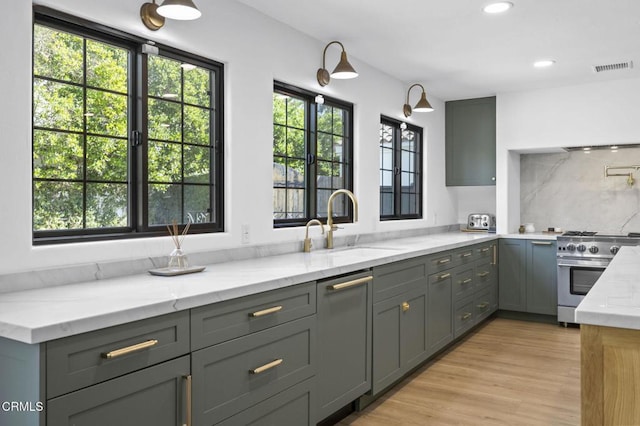 kitchen with light stone counters, a sink, high end stove, gray cabinets, and visible vents