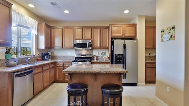 kitchen with a center island, a breakfast bar, stainless steel appliances, a sink, and light stone countertops