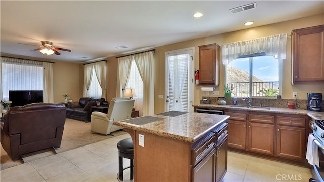 kitchen featuring visible vents, open floor plan, a center island, light stone countertops, and a sink